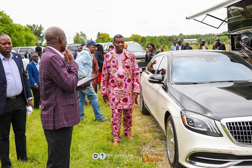 Pastor EA Adeboye walks beside black and white colored Mercedes-Maybach.