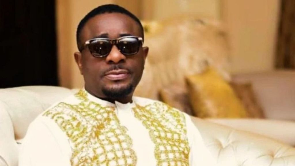 Emeka Ike sitted on a couch wearing black glasses