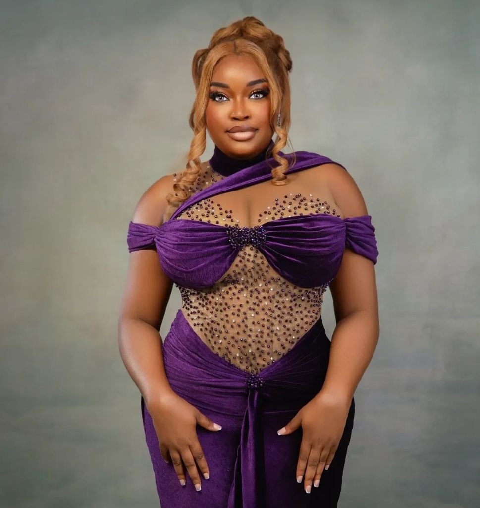 BBNaija star Chinwe standing against a gradient background, wearing an elegant purple dress with a unique bodice embellished with rhinestones. The dress features off-shoulder sleeves and a fitted silhouette that highlights her figure. Her hair is styled in braids swept to one side, adding to her sophisticated look.