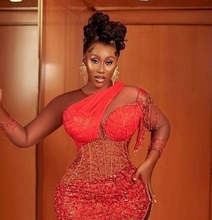 BBNaija Nelly wears a red lace dress with intricate patterns and a hairstyle with updo braids.