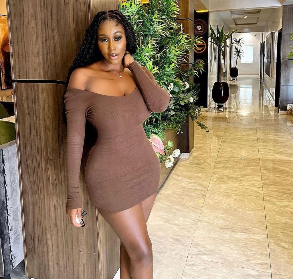 Nelly opts for an elegant brown dress that complements the natural greenery beside her.