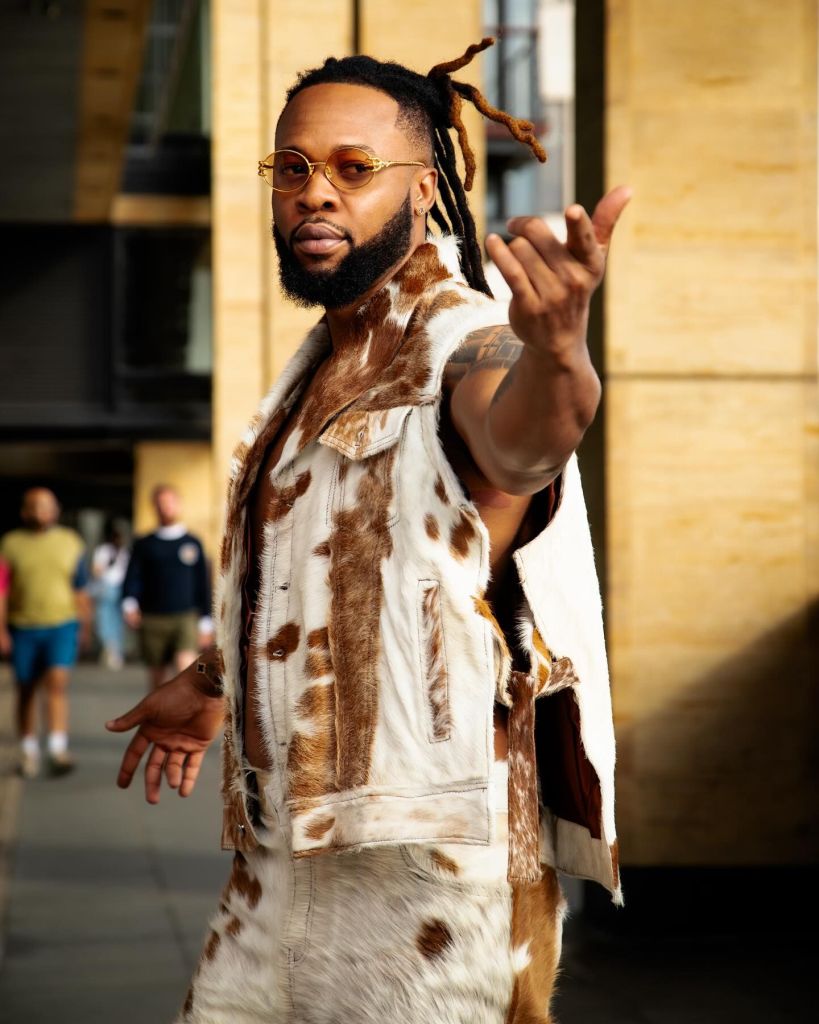 Flavour is captured in traditional Nigerian attire, including animal fur and leather, with an outdoor setting in the background.