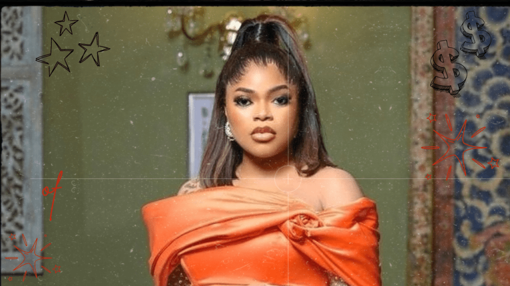 Bobrisky draped in an elegant orange attire stands against a textured backdrop, exuding a sense of style and mystery.