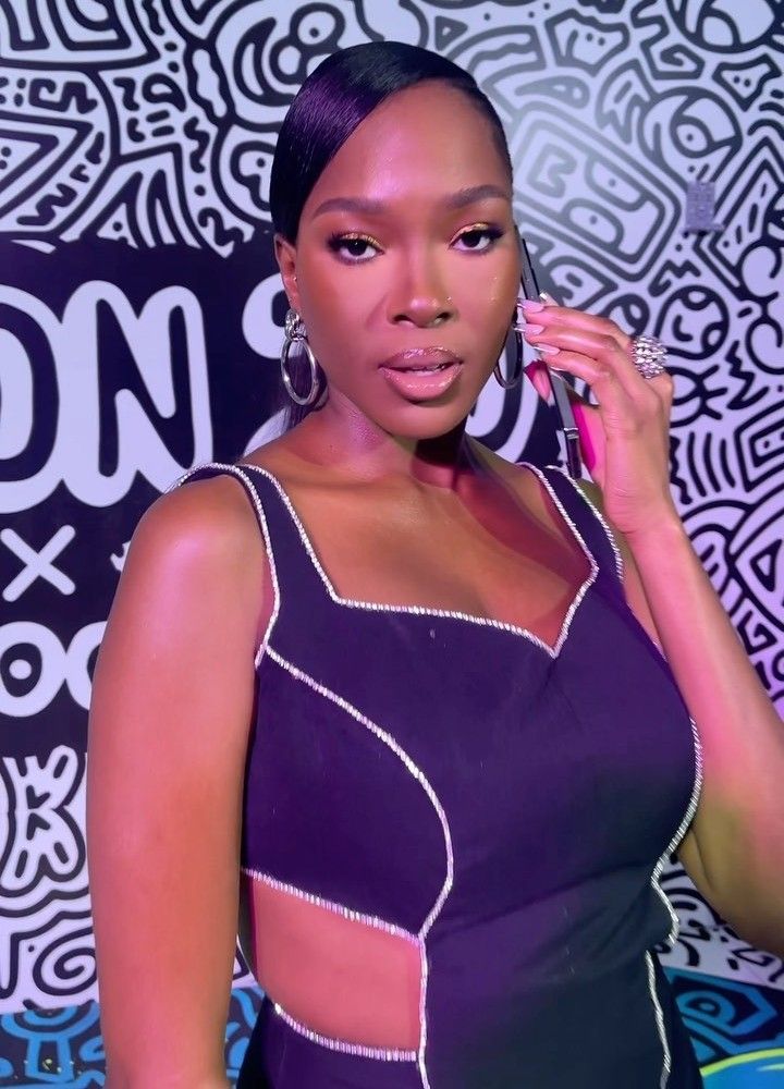 BBNaija star Vee is seen in a sleek black dress with silver accents and cut-out detailing. She has her hair styled in a smooth, side-parted updo, accessorizing with large hoop earrings and a confident pose.