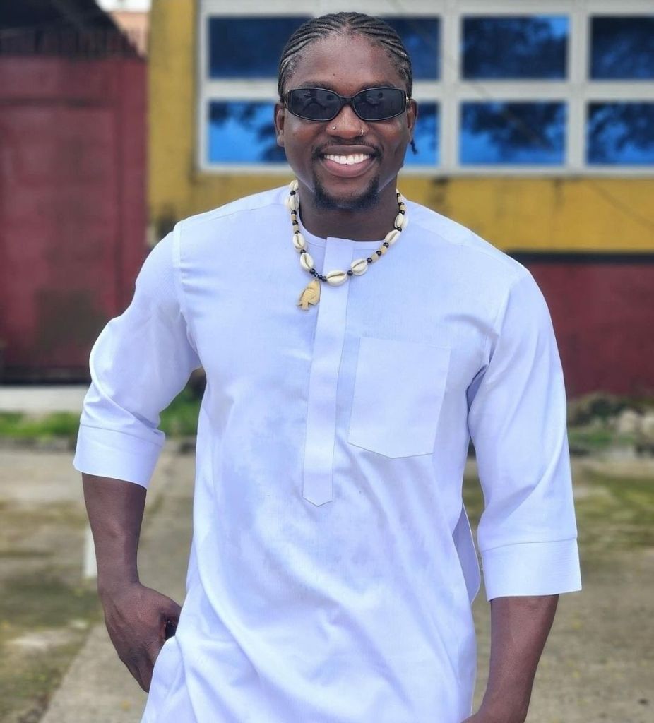 Verydarkman is smiling while wearing sunglasses and a traditional outfit, adorned with a necklace.