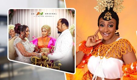 Actress Ini Edo dressed in traditional attire with vibrant orange fabric and intricate beadwork poses confidently. She wears a striking ornate headpiece and accessorizes with matching wristbands, set against a warm, orange background that enhances her joyful expression.