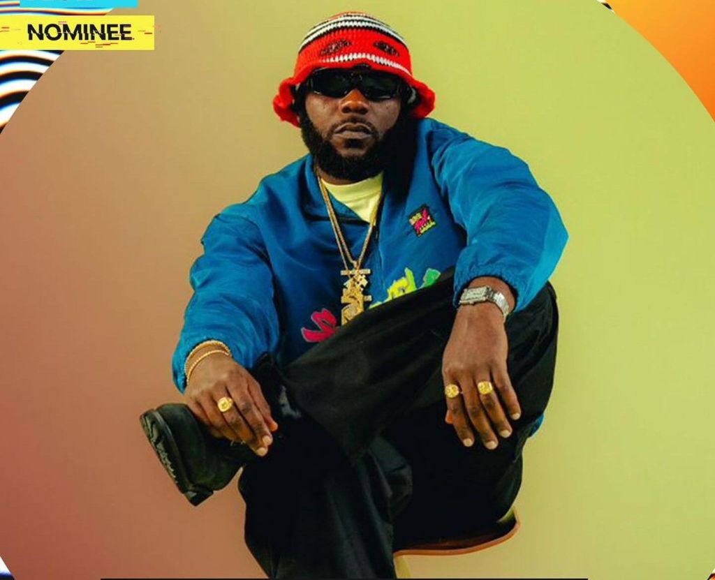 Odumodublvck sports a vibrant blue jacket and a red hat, exuding a stylish vibe.