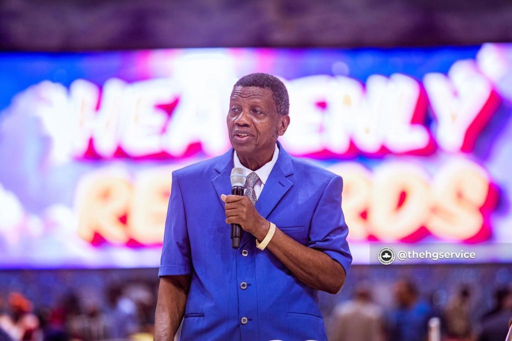 Pastor Adeboye is in a blue suit holding a microphone.