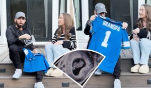 A heartwarming moment featuring rapper Eminem and his daughter, Hailie Jade, sitting together on a porch. Eminem is holding up a blue shirt that says "Grandpa" while Hailie smiles next to him. A sonogram showing a heart-shaped image is inset in the foreground, revealing Hailie's pregnancy announcement.