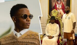 Wizkid in sunglasses and a patterned sweater on the left, while the Olu of Warri is seated in ornate attire, and Davido stands beside him on the right, dressed casually.