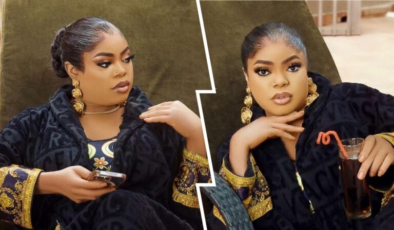 Bobrisky lounges comfortably, wearing a luxurious black robe with ornate gold details. He holds a phone and sipping a drink decorated with a straw, exuding confidence and style.