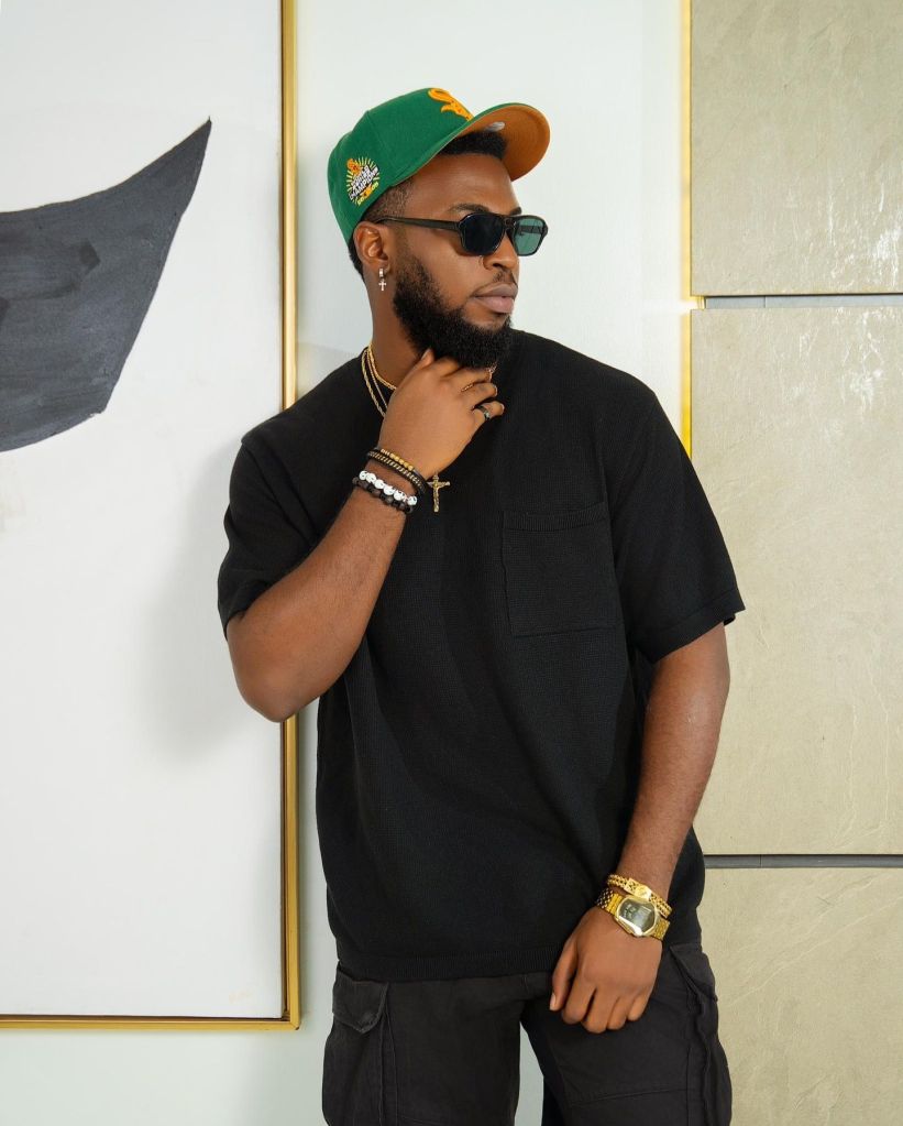 Zion wears a black shirt, sunglasses, and a green cap.