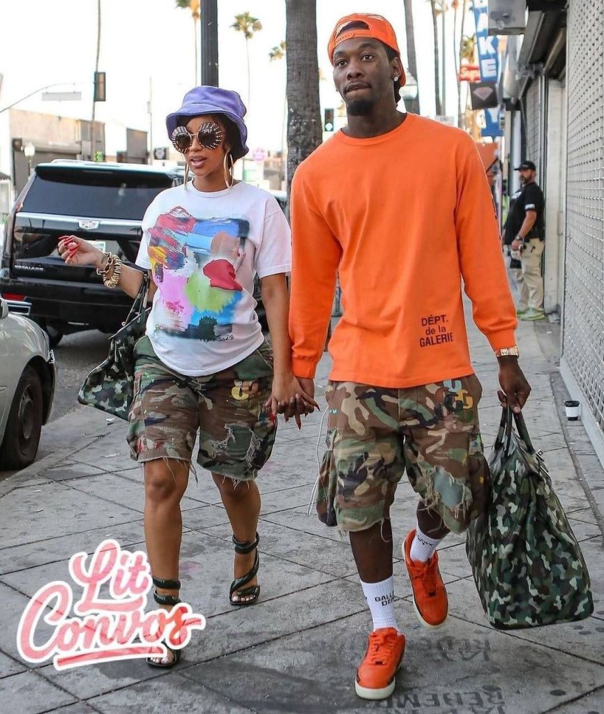 The scene captures rapper Offset and Cardi B, an estranged couple, strolling together on a city sidewalk lined with palm trees and parked cars. Offset sports a bold orange ensemble, including a cap, long-sleeve shirt with "DÉPT. de la GALERIE" text, camouflage shorts, and matching sneakers, while carrying a green duffel bag. Cardi B complements the look with a colorful abstract T-shirt, purple bucket hat, oversized sunglasses, and distressed camouflage shorts paired with strappy heels, also holding a matching bag. The text "Lit Convos" is overlaid in a playful pink font, adding a lively vibe to their coordinated street style.