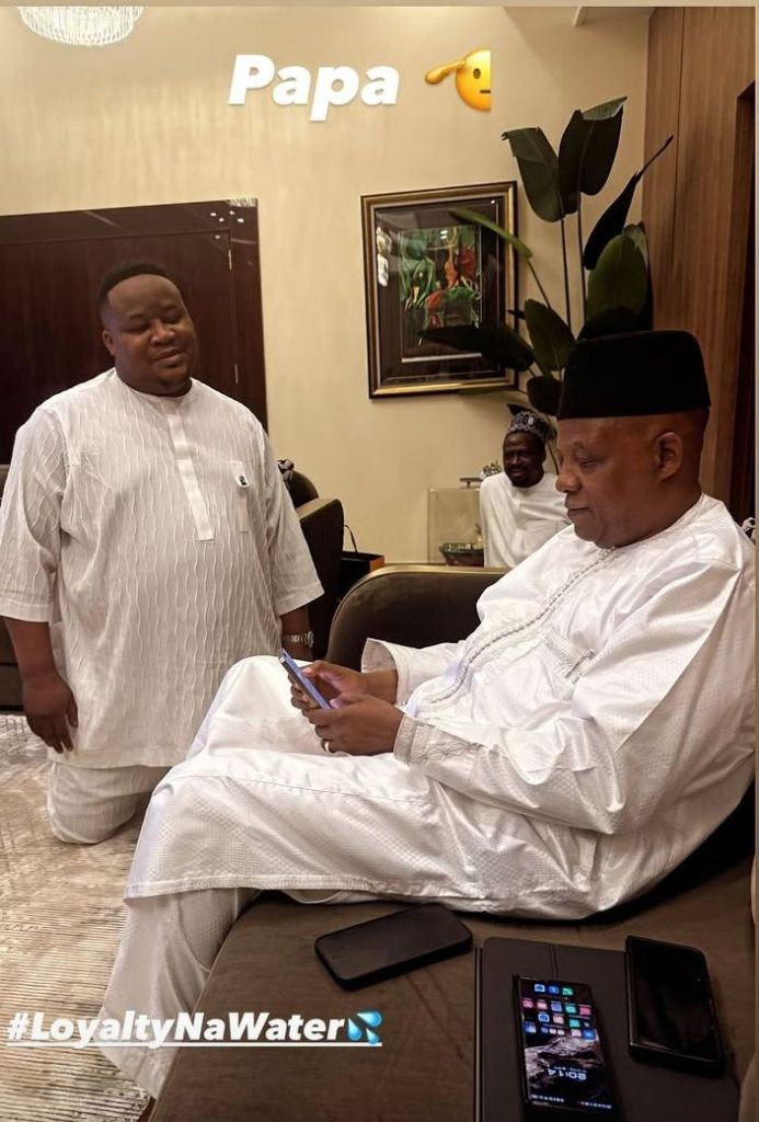 Cubana Chief Priest kneels before Vice President Shettima in a well-decorated room with the text "Papa" and a praying emoji above them, alongside the hashtag #LoyaltyNaWater. Two smartphones are placed on a table nearby.