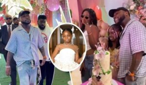 Singer Davido, dressed in a blue checkered shirt and distressed jeans, stands alongside his first baby mama, Sophia, and their daughter, Imade, who is elegantly dressed in white. The festive setting includes colorful balloons, floral decorations, and a tall, decorated cake, highlighting a joyful celebration.