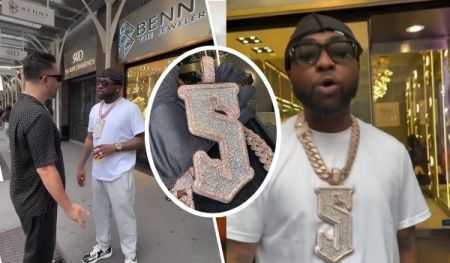 Singer Davido stands outside a jewelry store, wearing a white shirt and a large, ornate 5ive pendant necklace with a prominent "5" design, while conversing with another man. A close-up highlights the intricate detailing of the pendant, and another scene shows Davido inside the store, showcasing the luxurious setting.