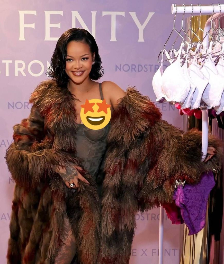 Rihanna stands in front of a Fenty x Nordstrom backdrop, wearing a luxurious multicolored fur coat over a sheer outfit, with a smiling emoji covering her chest. She accessorizes with a ring and poses near a display of white and purple bras.