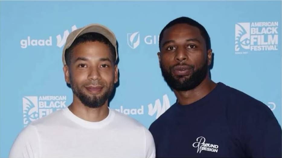 Actors Jussie Smollett and Jabari Redd pose together at the American Black Film Festival, with Jussie wearing a white t-shirt and beige cap, and Jabari in a dark blue "Sound Design" t-shirt, against a blue backdrop with festival logos.