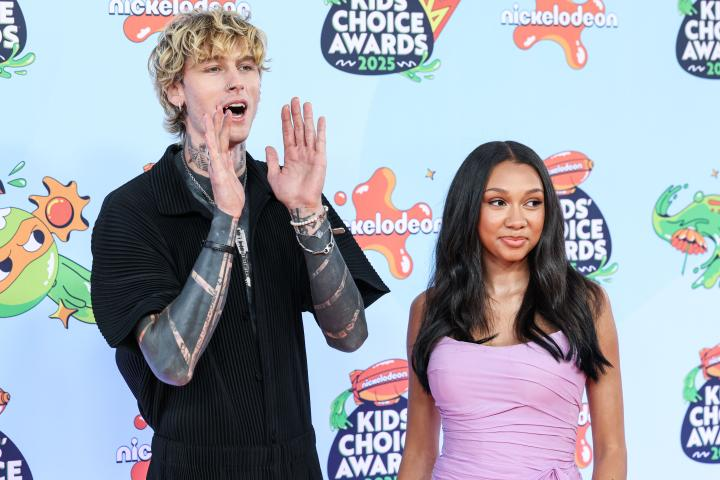Machine Gun Kelly and his daughter Casie attend the 2025 Nickelodeon Kids' Choice Awards, with Kelly in a sleek black outfit revealing his tattoos and Casie in a soft lavender dress, posing together against a colorful event backdrop.