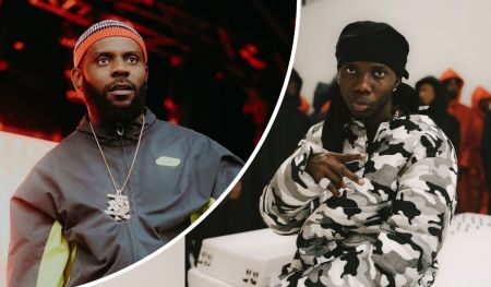 Odumodu Blvck appears on the left in a dark jacket with neon details, a patterned cap, and a bold chain, while Blaqbonez stands on the right in a camouflage jacket and black head covering, flashing hand signs with ring-adorned fingers against a vivid red-lit background.