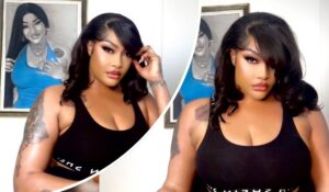 Angela Okorie poses in a black sleeveless top, revealing tattoos on her left arm, with a framed artwork of a woman in a blue top and flowing black hair displayed behind her.