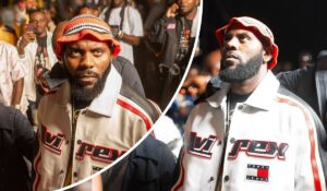 Rapper Odumodublvck stands out in a vibrant crowd, wearing a bold “VIREX” and “TOMMY JEANS” jacket paired with a colorful knit hat, as fans capture the moment around him.