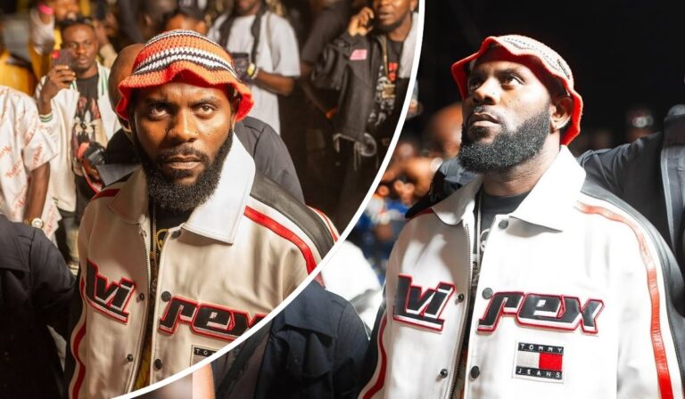 Rapper Odumodublvck stands out in a vibrant crowd, wearing a bold “VIREX” and “TOMMY JEANS” jacket paired with a colorful knit hat, as fans capture the moment around him.