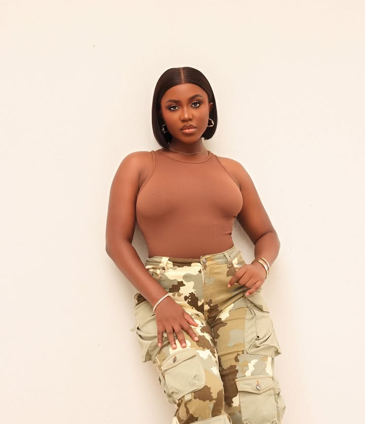 BBNaija star Wanni wears a brown sleeveless top with camouflage cargo pants, accessorized with hoop earrings and stacked bracelets, blending casual flair with bold, confident style.