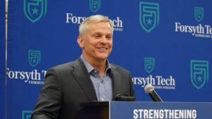 Governor Josh Stein speaking at a podium with a Forsyth Tech Community College backdrop, featuring the college's logo and the word "STRENGTHENING."