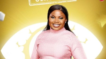 BBNaija Season 10 housemate Doris smiling in a patterned pink outfit against the signature Big Brother Naija eye logo backdrop.