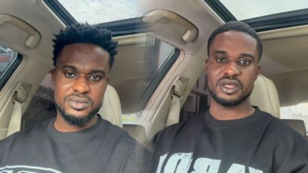 Scott Iguma appears seated inside a car, captured in two different moments wearing a black sweatshirt and speaking directly to the camera.