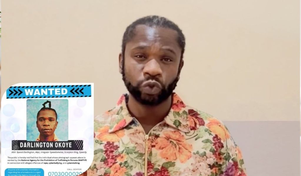 Rapper Speed Darlington, dressed in a vibrant floral shirt, stands beside a “WANTED” poster bearing his name and aliases, issued by NAPTIP in connection with serious allegations.