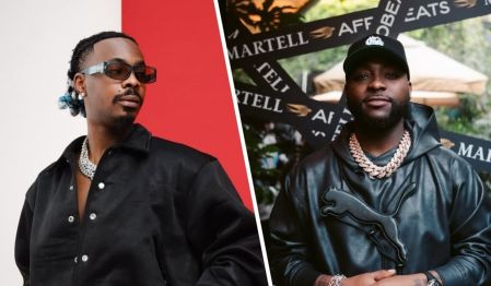 Young Jonn stands confidently in a black jacket adorned with silver buttons and a chunky chain necklace, while Davido sports a black leather Puma hoodie and matching chain, set against a backdrop featuring a Martell promotional banner.