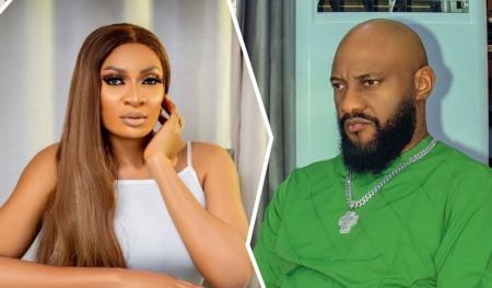 May Edochie appears poised in a white sleeveless top, resting her chin thoughtfully on her hand against a soft curtain backdrop. Opposite her, Yul Edochie sits in a green outfit with a silver chain and pendant, framed by gray drapes and a window, suggesting a contrast in mood and setting.