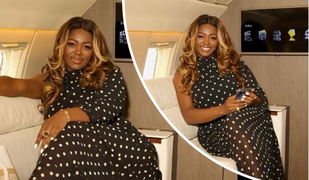 BBNaija star Ka3na exudes elegance aboard a private jet, dressed in a chic black polka dot dress with loose curls framing her face. She holds a smartphone, surrounded by a sleek interior and an entertainment screen, capturing a moment of luxury and style.