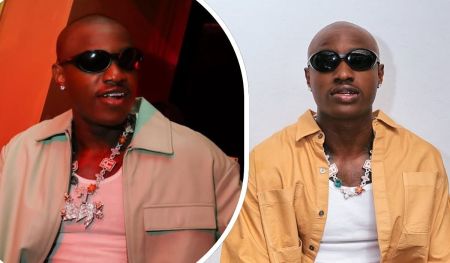 Ruger appears in two contrasting outfits that showcase his bold fashion sense. One look features a light jacket layered over a white tank top, while the other pairs a mustard button-up shirt with the same inner top. A distinctive charm necklace adds continuity and flair across both styles.