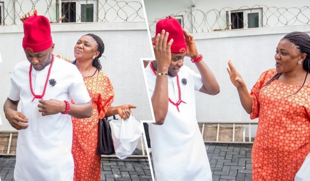 Ubi Franklin and his sister are seen in traditional attire, featuring white and orange outfits with red accessories, posing together outdoors near a barbed-wire fence, with one holding a bag and another gesturing expressively.