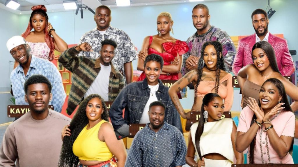 A group photo of BBNaija Season 10 housemates posing inside the Big Brother Naija house. The lineup features both male and female contestants in vibrant outfits, smiling and standing together in the well-lit lounge area.