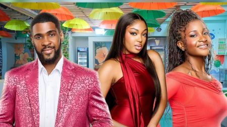 BBNaija Season 10 housemates Bright Morgan, Mide, and Big Soso posing inside the Big Brother Naija house, with Bright in a patterned pink suit, Mide in a red halter dress, and Big Soso in an off-shoulder red dress, all smiling towards the camera.
