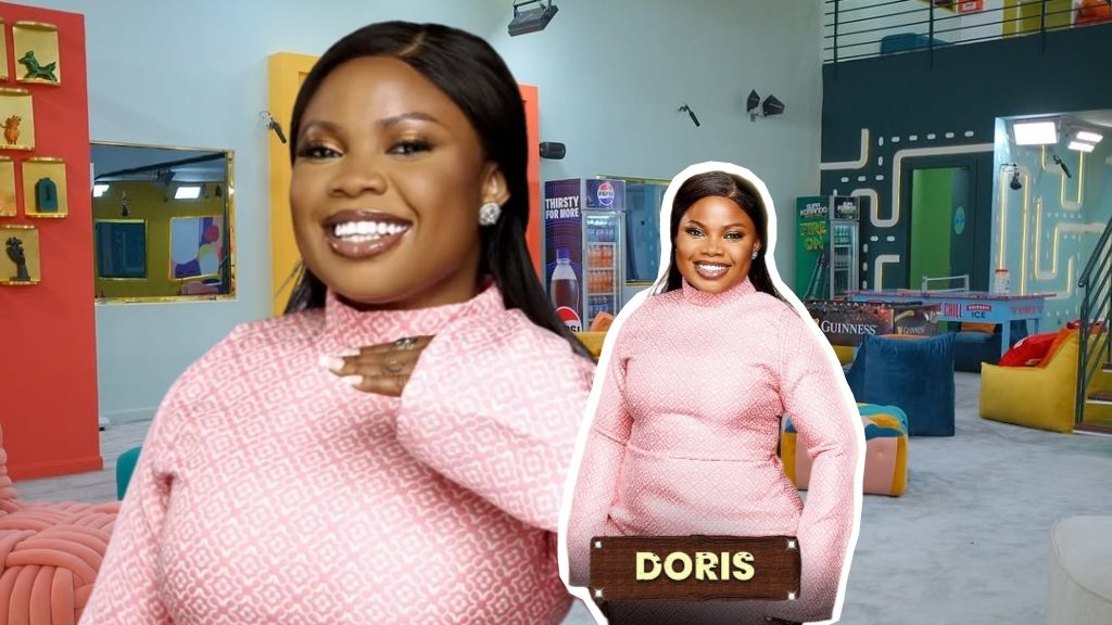 BBNaija Season 10 housemate Doris smiling in the Big Brother Naija house, dressed in a pink patterned outfit, with her official portrait card displayed beside her.