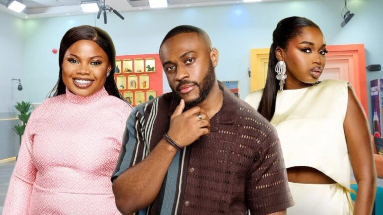 BBNaija Season 10 housemates Doris, Kola and Sabrina posing together inside the Big Brother Naija house. Doris is dressed in a pink patterned high-neck outfit, Kola in a brown striped shirt, and Sabrina in a cream two-piece with statement earrings.