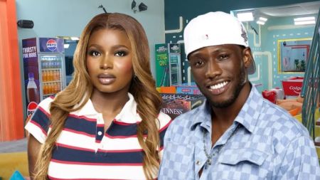 Big Brother Naija season 10 housemates Isabella and Kayikunmi posing together inside the colourful Big Brother house, with branded drinks and the Colgate game table visible in the background.