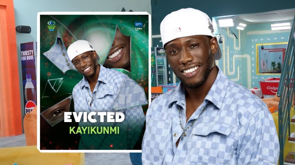 BBNaija Season 10 housemate Kayikunmi smiling in the Big Brother Naija house, with his official eviction card showing "Evicted Kayikunmi" placed beside him.