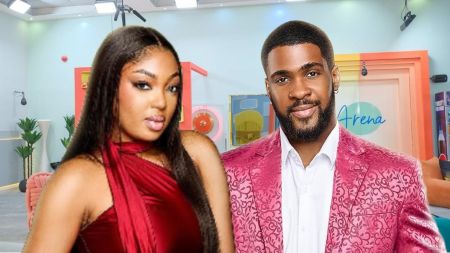 BBNaija Season 10 housemates Mide and Bright Morgan pose inside the house. Mide stuns in a bold red halter dress, while Bright Morgan looks dapper in a patterned pink suit jacket paired with a white shirt.