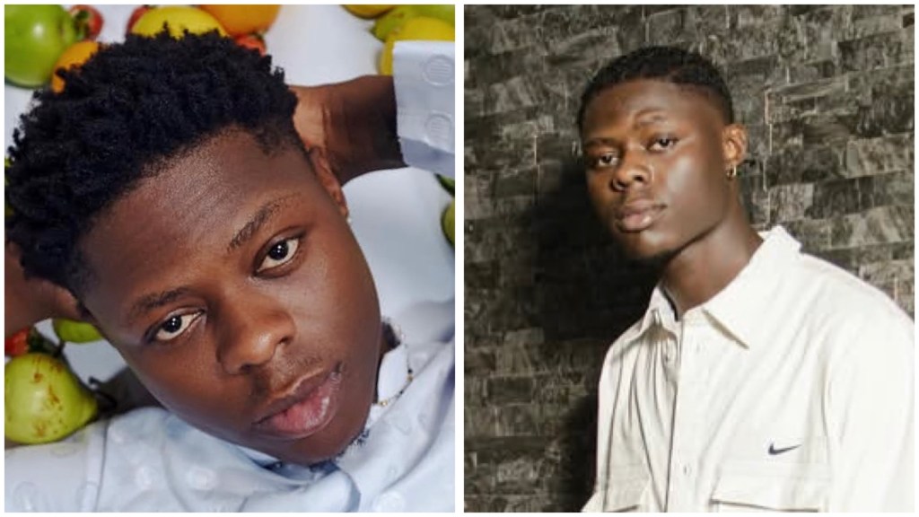 Late Nigerian singer Mohbad, head leaned back among fruits, standing in a white Nike shirt against a dark stone wall.