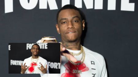 American rapper Soulja Boy poses on the red carpet at a Fortnite-themed event, wearing a white shirt with red graphics and multiple gold chains, while flashing hand signs and looking confidently at the camera.