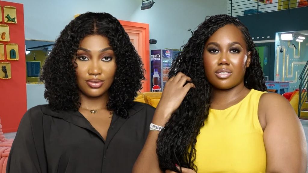 BBNaija Season 10 housemates Sultana and Gigi pose inside the Big Brother Naija house, with Sultana in a black outfit and Gigi in a yellow sleeveless dress.