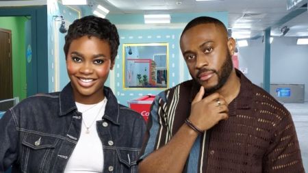 BBNaija Season 10 housemates Dede and Kola pose together inside the house. Dede smiles in a denim jacket over a white top, while Kola stands beside her with a thoughtful look, dressed in a brown patterned shirt. The colourful house setting can be seen in the background.