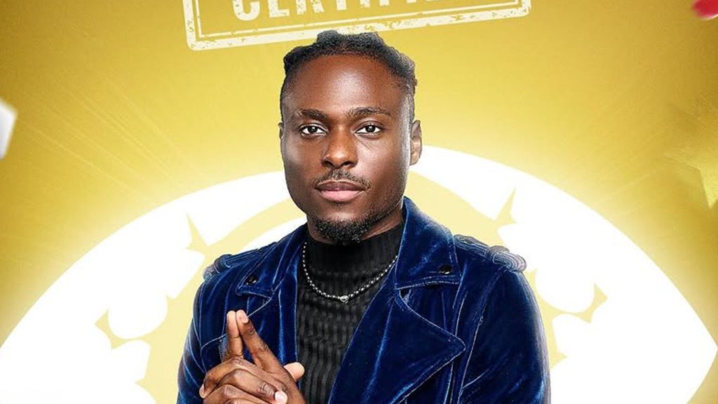 BBNaija Season 10 housemate Dede poses in a denim jacket, smiling in her official portrait against a gold background.
