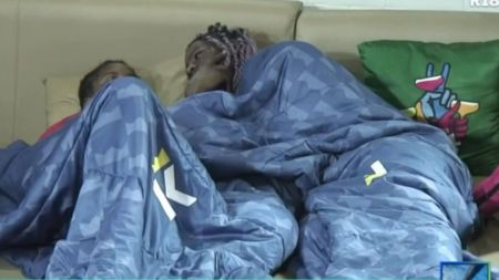 BBNaija housemates Isabella and Koyin lie under a blue duvet on a couch, facing each other during a quiet moment in the house.